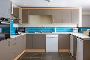 Cozinha moderna com armários cinza, lava-louças, micro-ondas e um recipiente para pão.