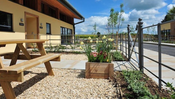 A modern building with a wooden exterior, a picnic table, and a garden area with flowers and plants. - Sleeps 8, 4 Bedrooms, Dogs Welcome, No Smoking, Wood burner, Wi-Fi*, Garden, Games Room (Cheltenham)