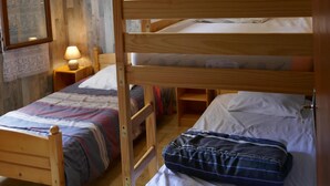 A room with two wooden bunk beds, a wooden floor, a wall-mounted lamp, and a framed picture on the wall.
