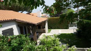 A house with a tiled roof, a covered porch, and a well-maintained garden with various plants and a bench.