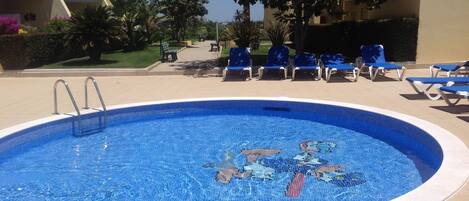 A swimming pool with a mosaic design, surrounded by lounge chairs and a paved deck.