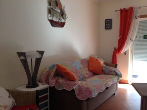Una sala de estar acogedora con un sofá, un adorno de barco en la pared y una ventana con cortinas.