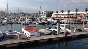 Un port de plaisance où sont amarrés de nombreux bateaux, une jetée et un bâtiment, avec des palmiers en arrière-plan.