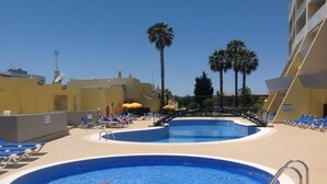 Un espace piscine comprenant deux piscines, des chaises longues et des palmiers.