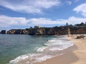 A coastal beach with clear waters, rocky cliffs, and a building on the cliff. - 2 bed apt.24 hr. reception security. A/C.five minutes walk to beach /marina. (Lagos)