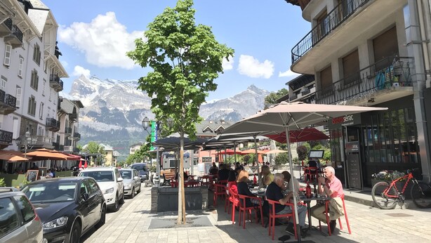 A café with outdoor seating, a tree, and a mountain backdrop.