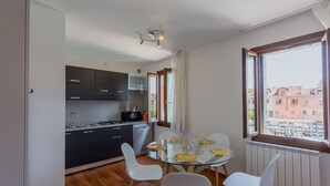 A modern kitchen with dark cabinets, a glass dining table, and white chairs. - Venice Appartament Salini II (Venezia)