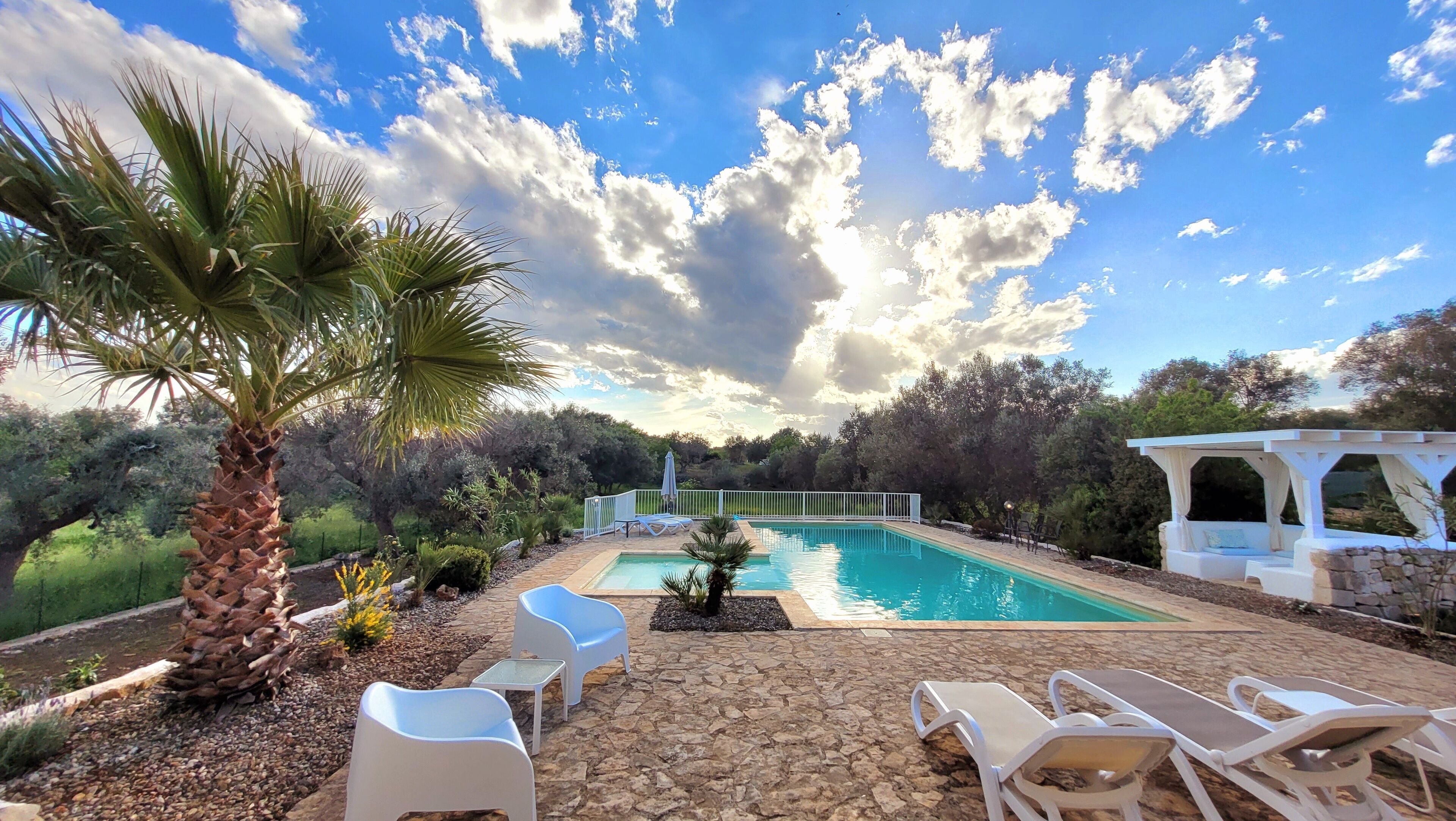Una piscina con sillones de descanso y una pérgola.