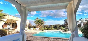 A covered outdoor swimming pool with lounge chairs and a view of a bridge and trees. - Modern Villa, Pool, Air Cond., Veranda, BBQ, outdoor Kitchen, outrdoor Shower (Ostuni)