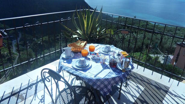 A table set with breakfast items on a balcony overlooking a coastal landscape.