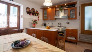 A kitchen with wooden cabinets, a central island, a sink, and a stove. There is a dining table with a placemat and a bowl of fruit.