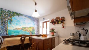 A kitchen with a dining area, a painting on the wall, a stove, and a coffee maker.