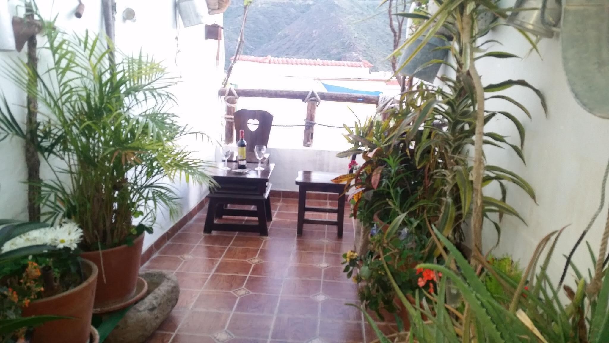 A patio with a tiled floor, a table, and chairs, surrounded by potted plants.