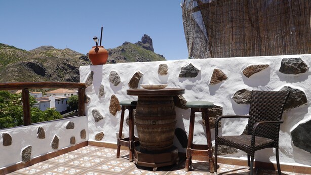 Eine Terrasse mit einer Steinmauer, einem Holztisch mit einer Schüssel und einem Korbstuhl.