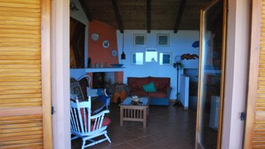 Una sala de estar acogedora con techo de madera, una mecedora blanca, un sofá rojo y una mesita.