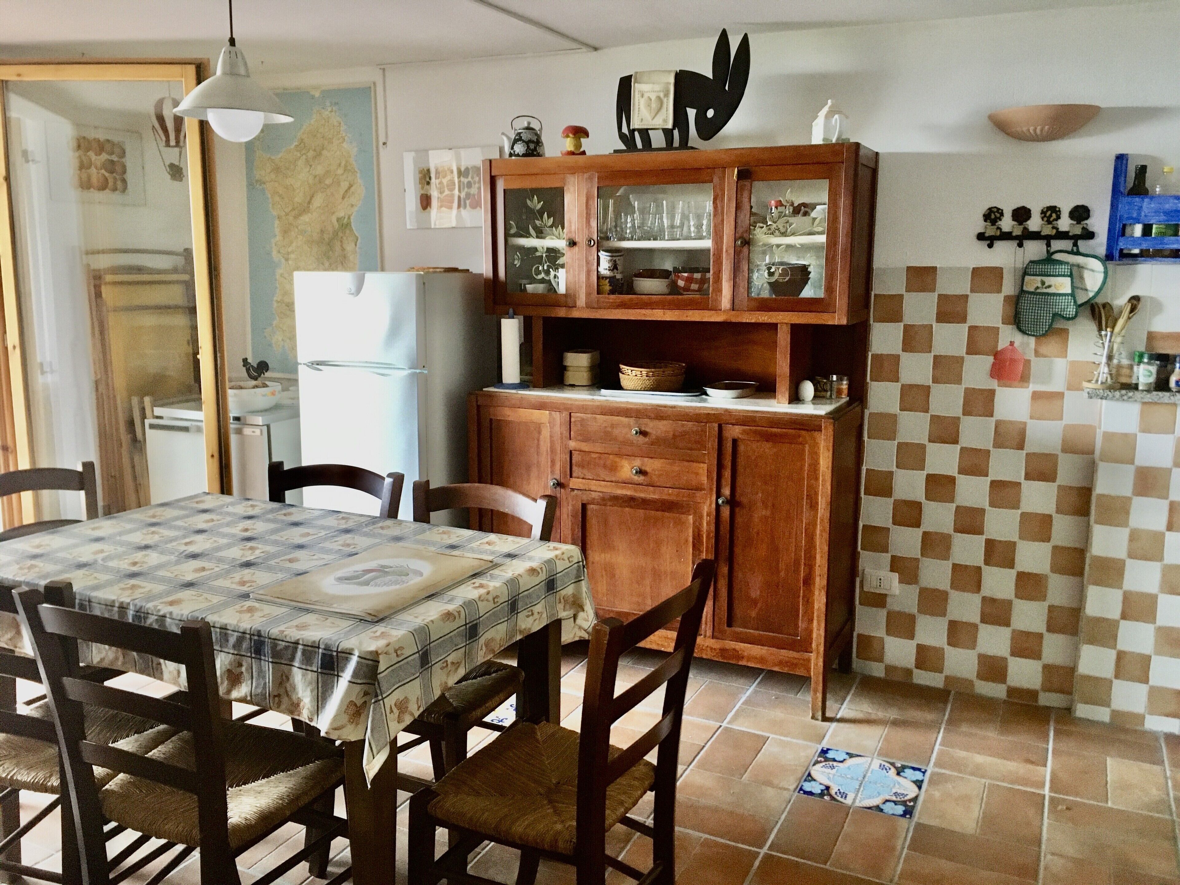 A dining area with a table set for four, wooden chairs, a cabinet with glass doors, and a tiled backsplash.