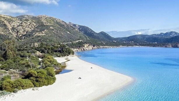 Una playa con aguas turquesas cristalinas y arena blanca, rodeada de colinas.