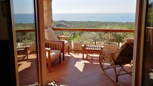 Un balcón con mobiliario de madera, vista al mar y cielo despejado.
