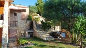 Un edificio de piedra con techo de tejas, un pequeño jardín con una palmera y un cielo despejado.