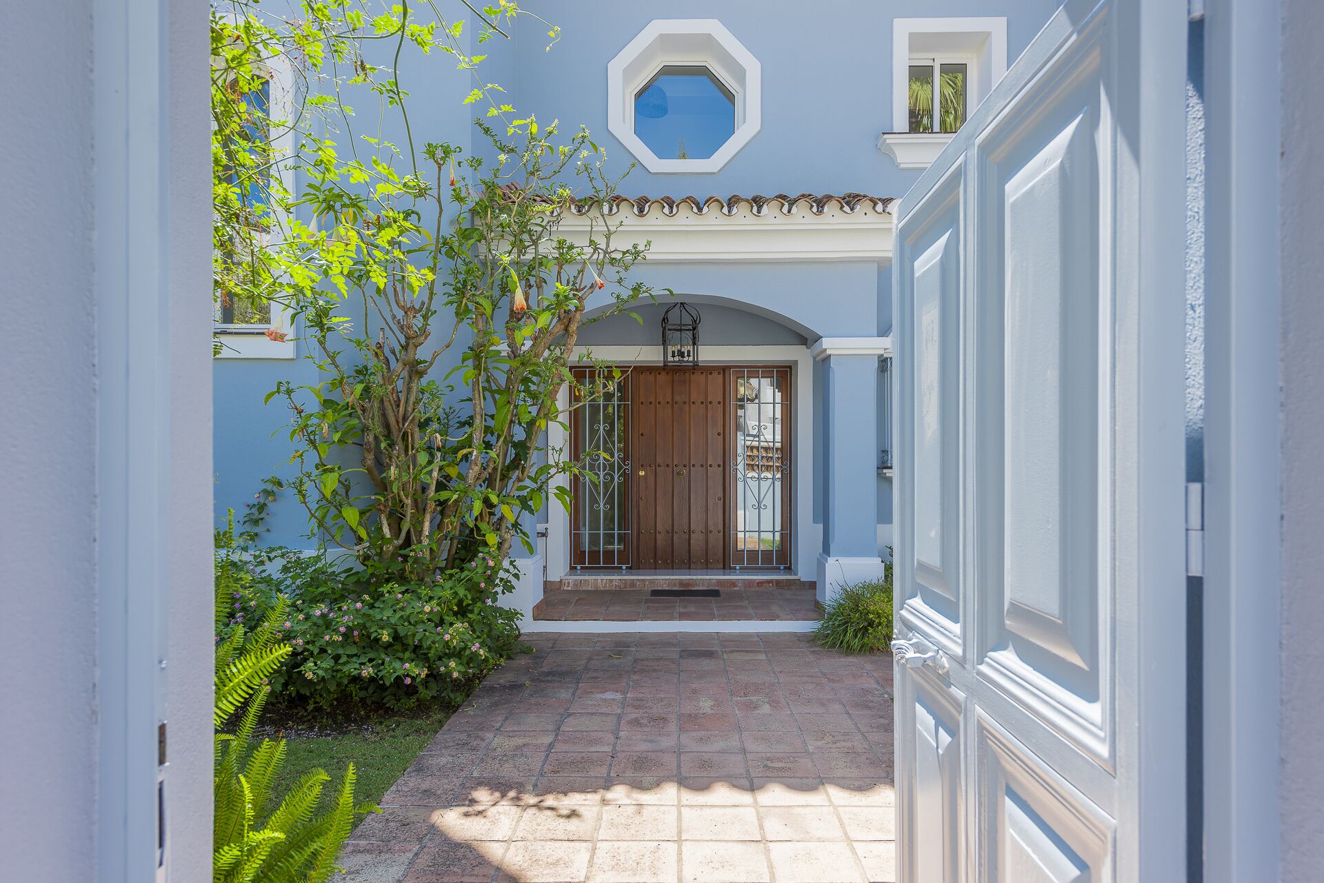 A narrow pathway leading to a house entrance with a wooden door and a small balcony.