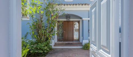 A narrow pathway leading to a house entrance with a wooden door and a small balcony.
