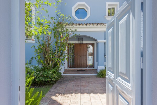 A narrow pathway leading to a house entrance with a wooden door and a small balcony.