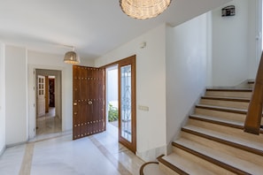 A hallway with a wooden door, a staircase, and a hanging light fixture.