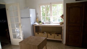 A kitchen with a wooden table, a white refrigerator, wicker baskets, and a window with a view of greenery.