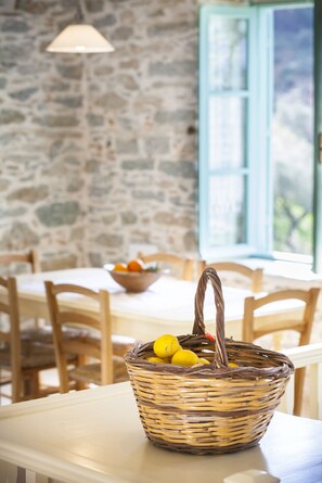 Un panier en osier contenant des citrons, posé sur une table dans une pièce aux murs de pierre et aux chaises en bois.