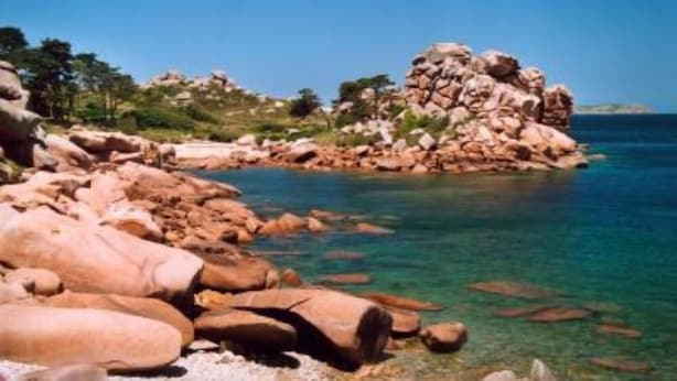 Un paysage côtier rocheux, avec des eaux d’un bleu limpide et une petite île couverte d’arbres.