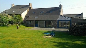 Une maison en pierre avec un toit en pente, une véranda en verre et une cour gazonnée.