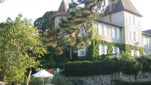 Um grande edifício de pedra com piscina, rodeado por vegetação e algumas espreguiçadeiras.