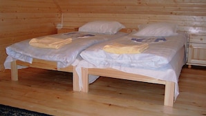 Una cabaña de madera con dos camas individuales, cada una con un colchón blanco y una manta doblada.