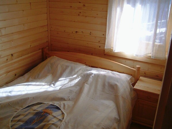 A single bed in a wooden cabin room with a window and a small wooden nightstand.