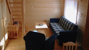 Una cabaña pequeña con interior de madera, un sofá, una mesa y una silla.