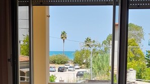 Ein Balkon mit Blick auf geparkte Autos und Palmen, eine Couch und Kübelpflanzen.