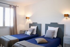 A hotel room with two beds, each with a headboard, a bedside table, and a lamp.
