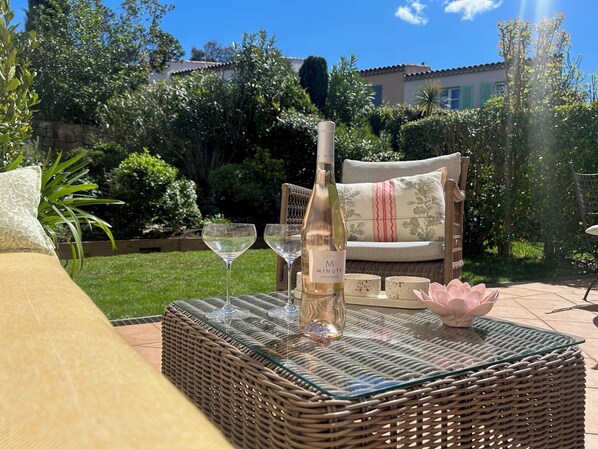A wicker table with a bottle of wine, two wine glasses, and a decorative bowl.