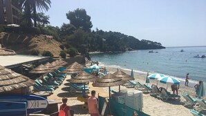 A beach with sun loungers and umbrellas, a rocky hillside in the background, and a clear blue sea. - Beautiful  Family Holiday Home  (La Môle)