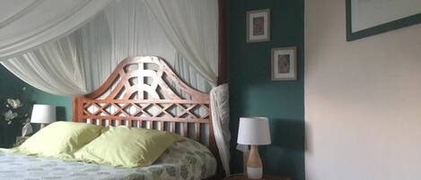 Een bed met houten hoofdbord, een nachtkastje met een lamp en een wand met ingekaderde foto's.