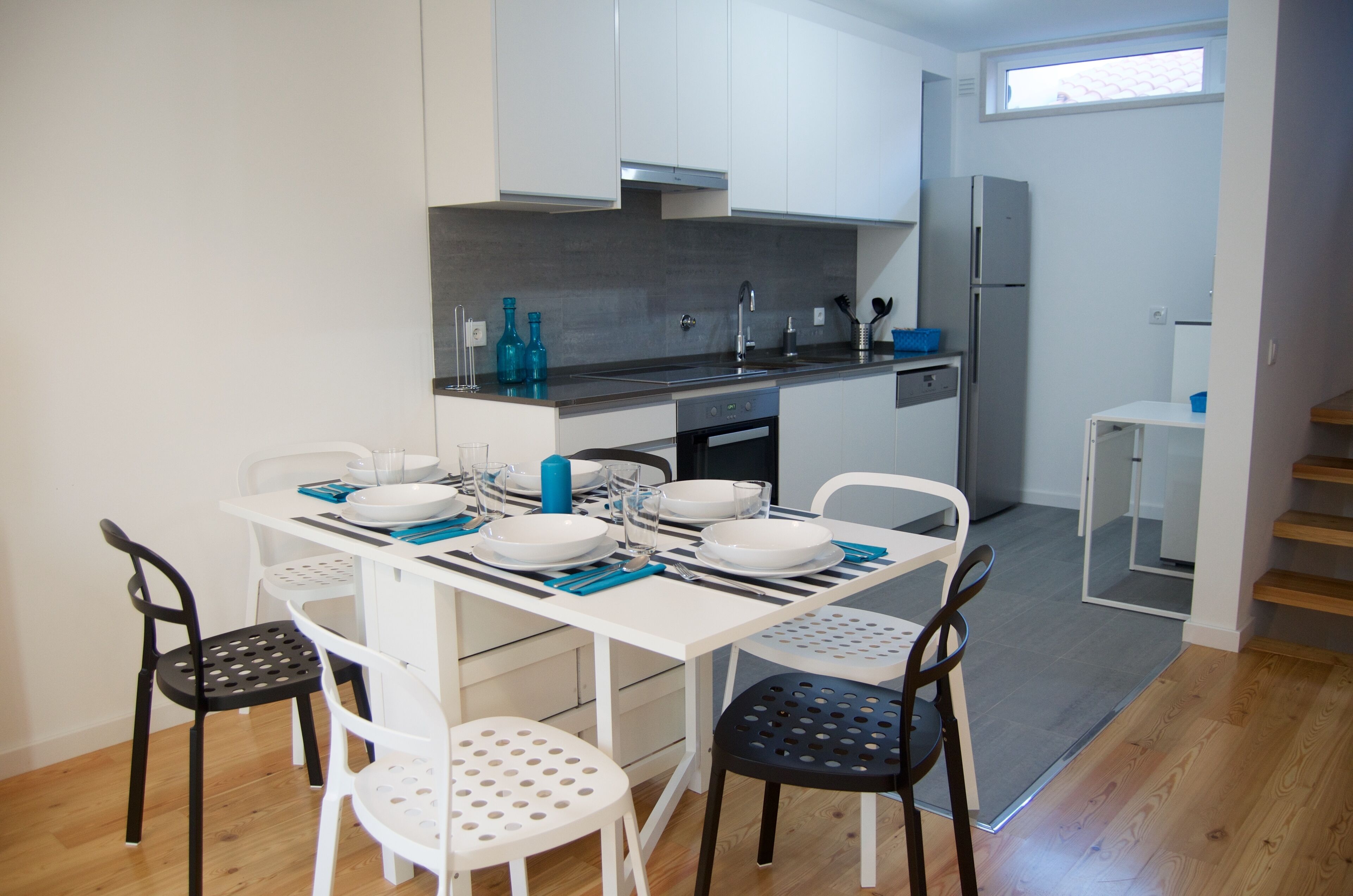 Een moderne keuken met witte kastjes, een roestvrijstalen spoelbak en een ingebouwde oven. Er staat een eettafel gedekt met borden, kommen en bestek.
