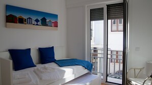 A room with a bed, a bench, a chair, a painting, and a sliding glass door to a balcony. - House in the Historic Center of Cascais (Cascais)