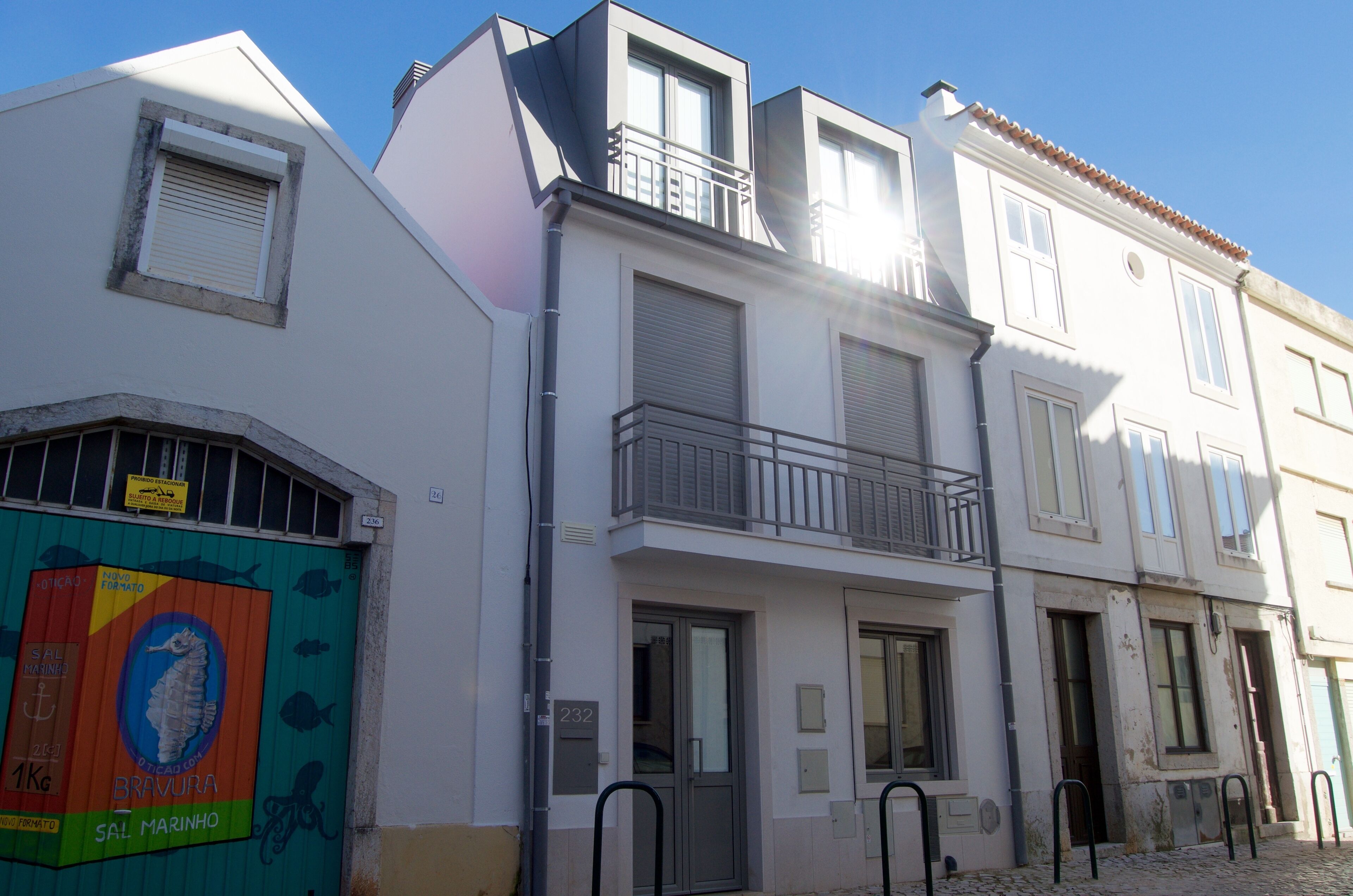 Un edificio a più piani con un balcone al secondo piano, un'auto in un garage con una pubblicità colorata e un cielo azzurro limpido.