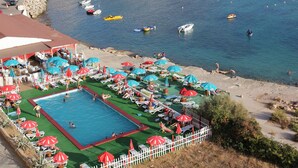Une piscine entourée d’une clôture blanche, avec des chaises longues et des parasols, et des bateaux amarrés à proximité.