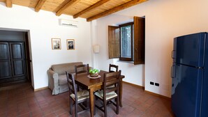 A compact kitchen with a wooden table, chairs, a blue refrigerator, a window with a wooden shutter, and a door with a dark wooden panel. - Farmhouse with pool between oranges and lemons trees (Mirto)