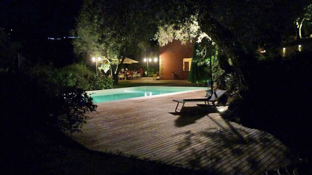 A wooden deck with a pool and lounge chairs, surrounded by trees and a building with lights. - Farmhouse with pool between oranges and lemons trees (Mirto)