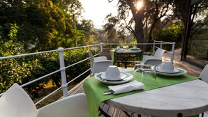 An outdoor dining area with white chairs and round tables, set against a backdrop of lush greenery and trees. - Farmhouse with pool between oranges and lemons trees (Mirto)