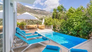 A pool area with lounge chairs and umbrellas, surrounded by greenery and mountains. - Villa With Private Heated Pool(optional extra) And Sea Views (Kalkan)