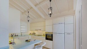A modern kitchen with white cabinetry, a central island with bar stools, a built-in oven, and pendant lighting. - Villa With Private Heated Pool(optional extra) And Sea Views (Kalkan)