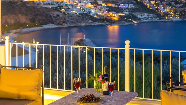 A balcony with a table set for two, overlooking a coastal town at dusk. - Villa With Private Heated Pool(optional extra) And Sea Views (Kalkan)